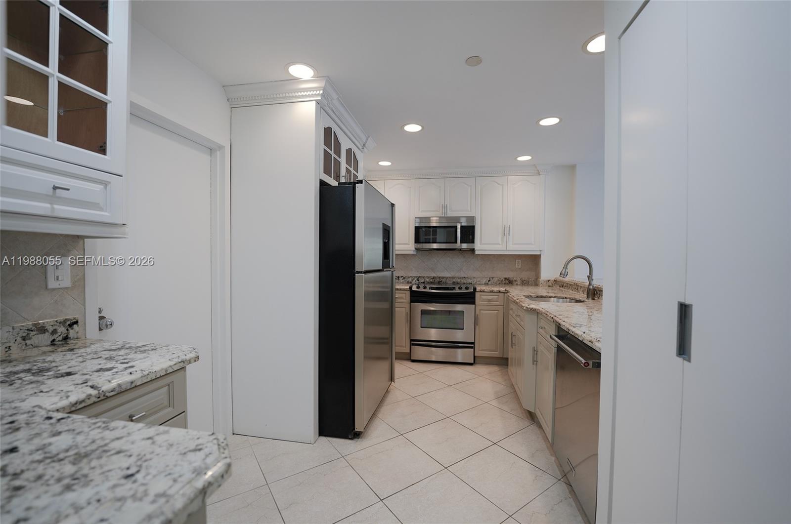 A kitchen features white cabinets, granite countertops, stainless steel appliances, and light-colored tile flooring — 151 Crandon Blvd # 320, Key Biscayne FL 33149, KEY BISCAYNE, FL