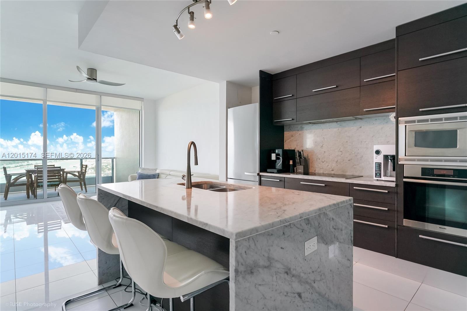 A modern kitchen features a marble island, dark wood cabinetry, and a balcony with ocean views — 900 Biscayne Blvd # 3407, Miami FL 33132, MIAMI, FL