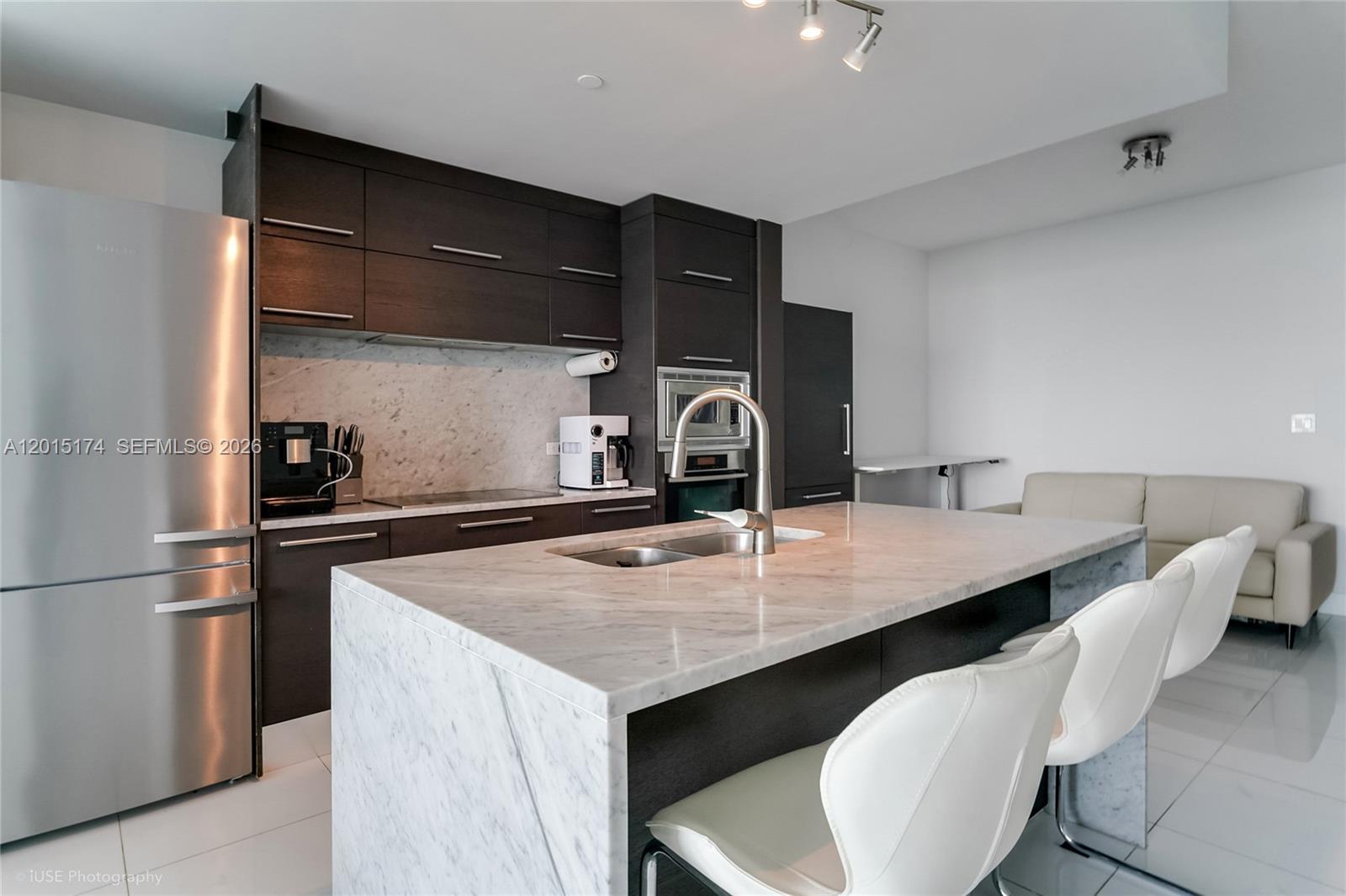 A modern kitchen features dark wood cabinetry, a marble island with seating, and stainless appliances — 900 Biscayne Blvd # 3407, Miami FL 33132, MIAMI, FL