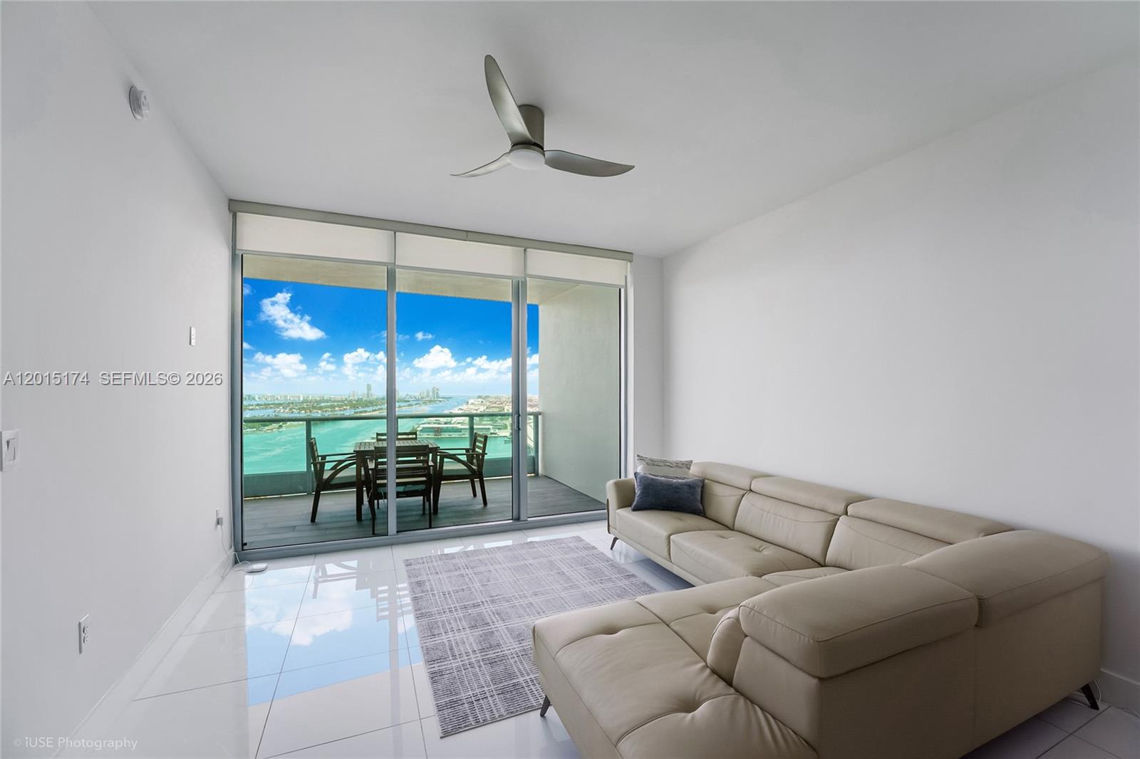 A living room with white tile floors, a beige sectional sofa, and a balcony view — 900 Biscayne Blvd # 3407, Miami FL 33132, MIAMI, FL