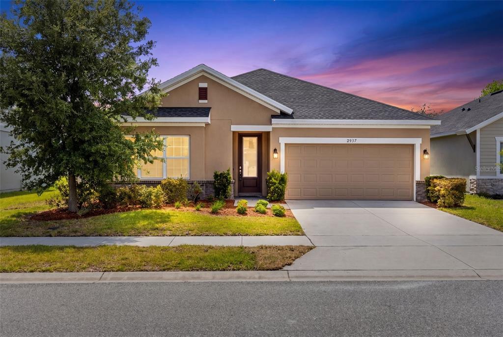 A single-story house with a tan stucco exterior, a two-car garage, and a front lawn — 2937 DEERBERRY LANE, CLERMONT, FL