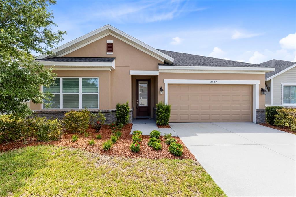 A single-story house with a tan stucco exterior, a two-car garage, and a front garden — 2937 DEERBERRY LANE, CLERMONT, FL