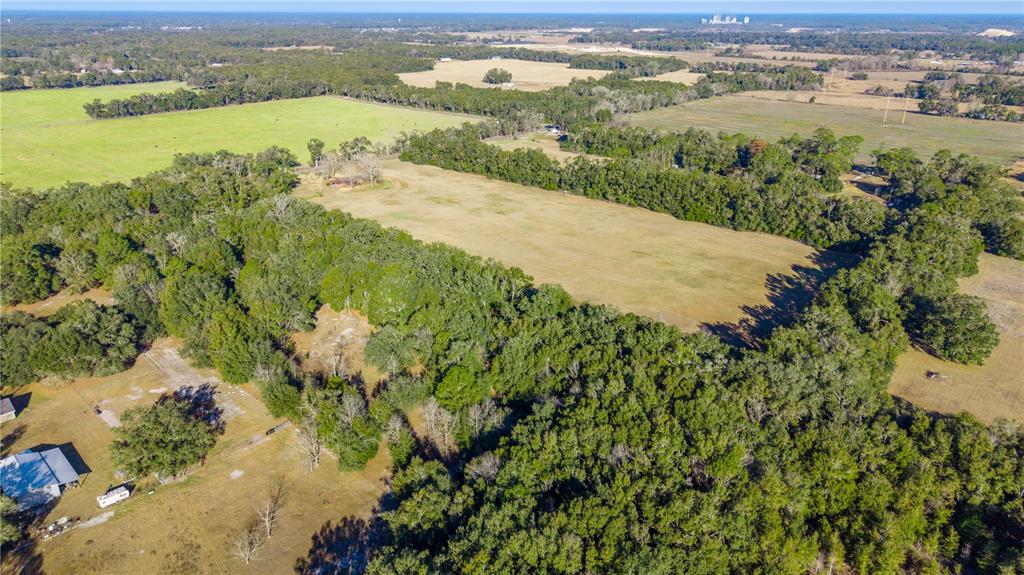 An aerial view shows a large, rectangular grassy field surrounded by dense forest and pastures — 0000 SW 202 STREET, NEWBERRY, FL