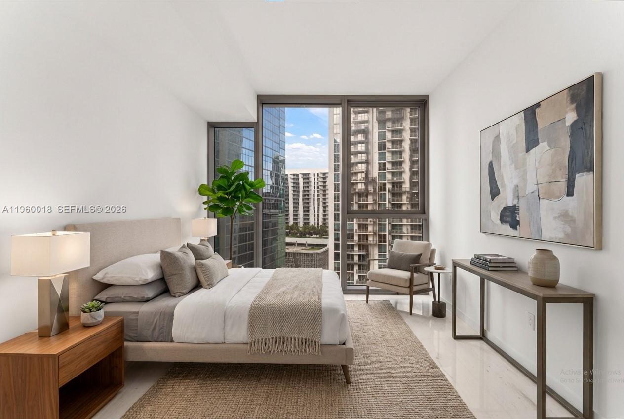 A modern bedroom features a bed, a console table, and floor-to-ceiling windows overlooking city buildings — 300 BISCAYNE BLVD WAY # 2009, Miami FL 33131, MIAMI, FL