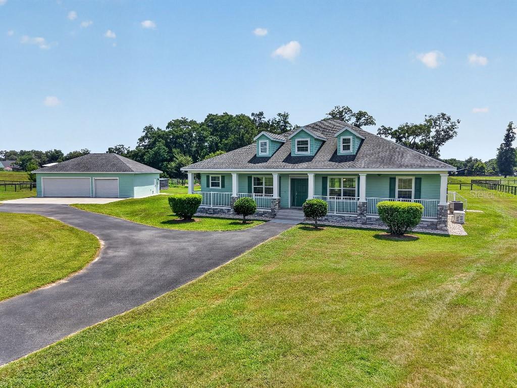 A light green house with a front porch and a detached garage sits on grass — 2556 NE 120TH STREET, ANTHONY, FL