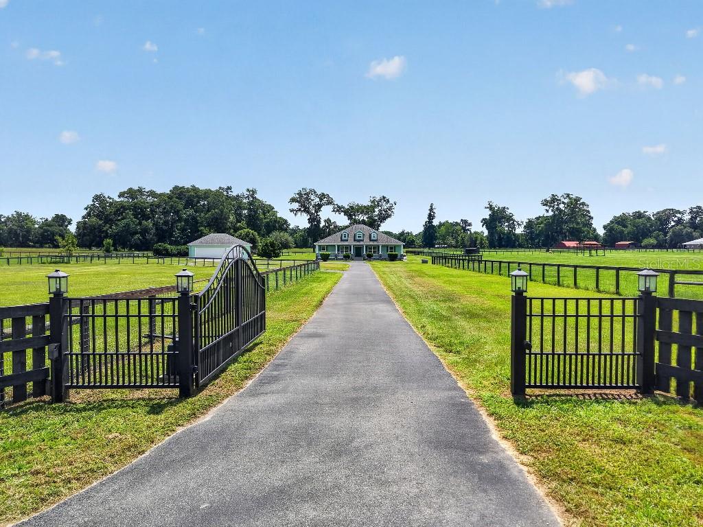 A long paved driveway leads through an open gate toward a house in a field — 2556 NE 120TH STREET, ANTHONY, FL