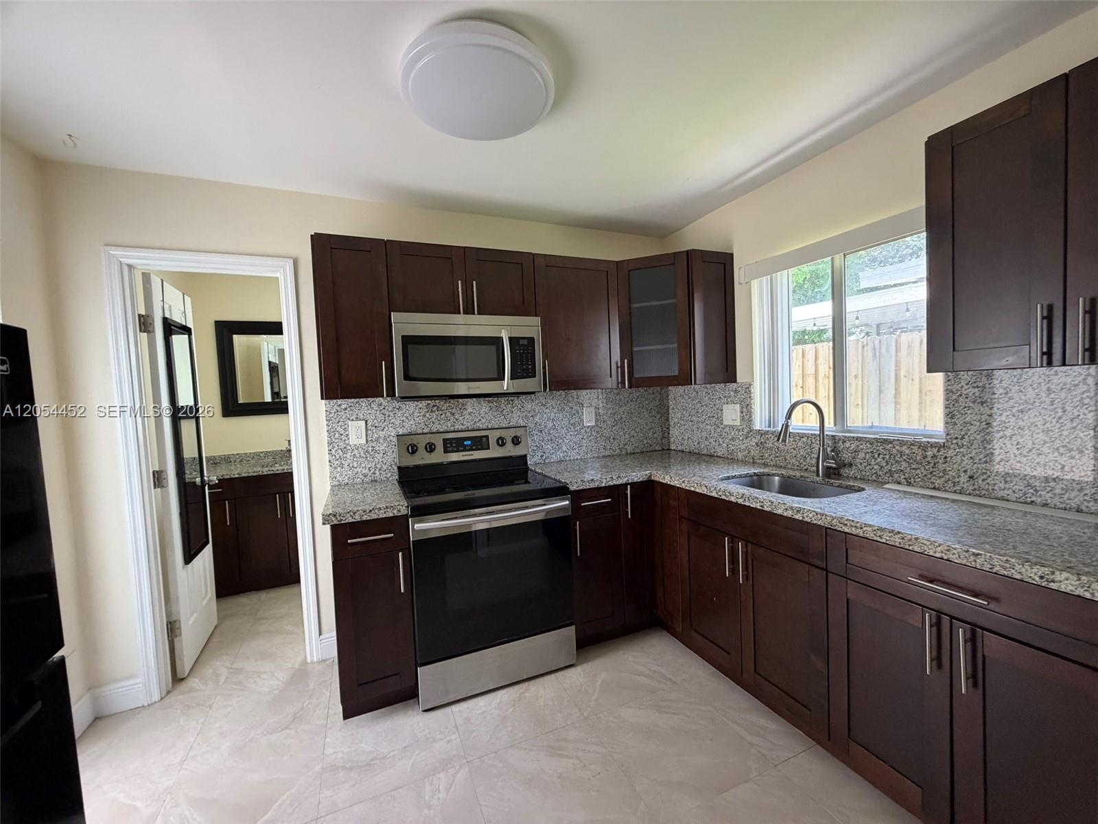 A kitchen features dark wood cabinets, granite countertops, stainless steel appliances, and tile flooring — 226 NE 25th Ave # 2, Pompano Beach FL 33062, POMPANO BEACH, FL