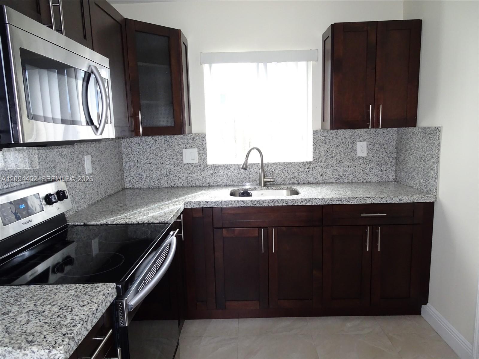 A kitchen features dark wood cabinets, granite countertops, a stainless steel microwave, and a stove — 226 NE 25th Ave # 2, Pompano Beach FL 33062, POMPANO BEACH, FL