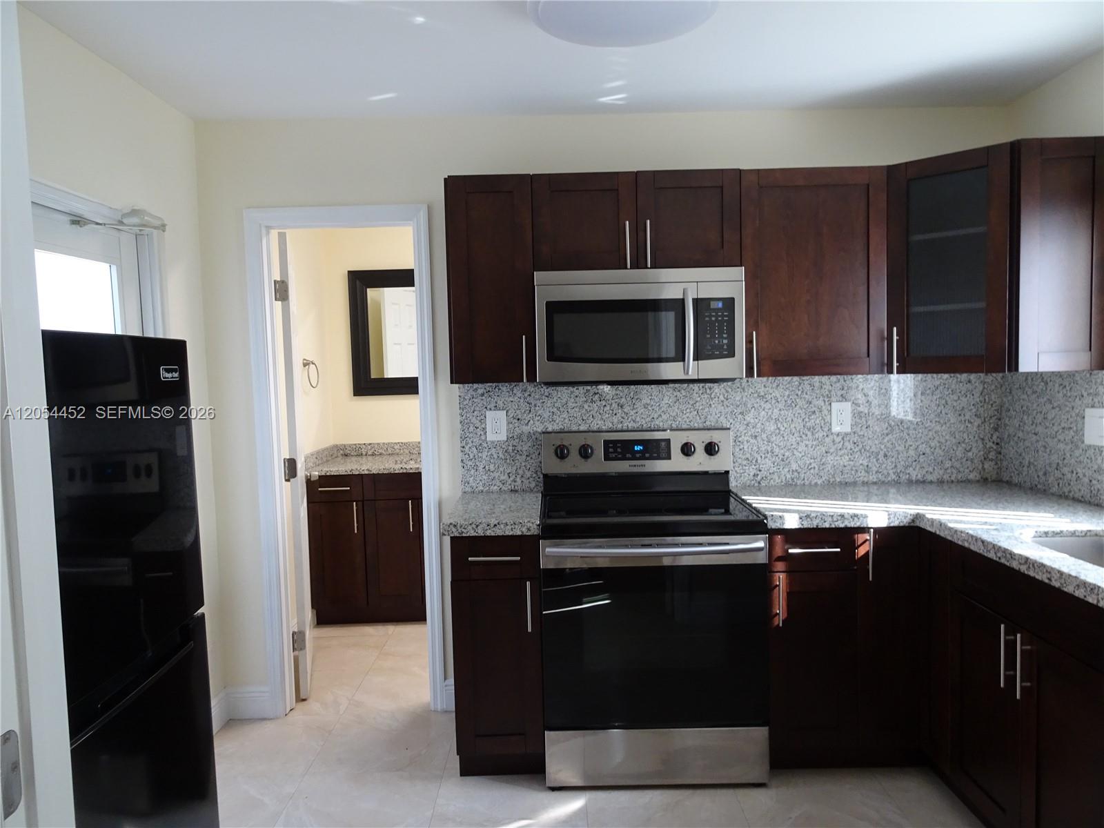 A kitchen features dark wood cabinets, granite countertops, stainless steel appliances, and an adjacent bathroom — 226 NE 25th Ave # 2, Pompano Beach FL 33062, POMPANO BEACH, FL