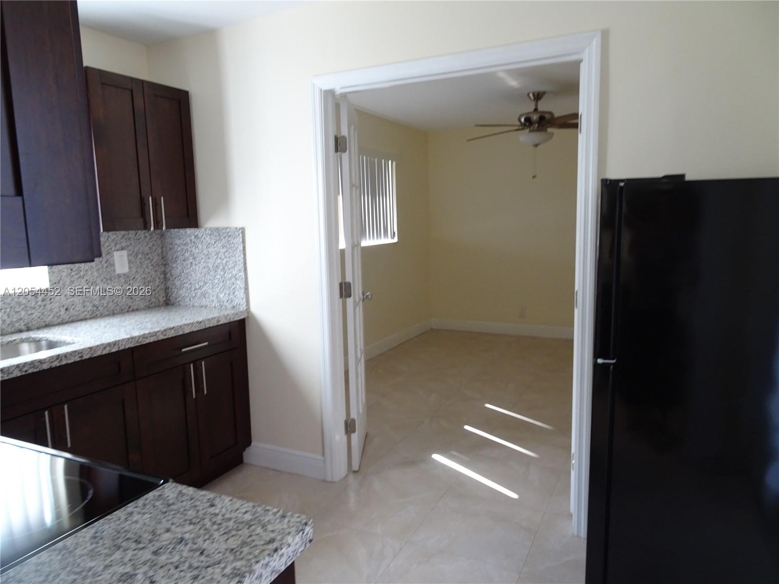 A kitchen with dark cabinets and granite countertops opens into a room with tile floors — 226 NE 25th Ave # 2, Pompano Beach FL 33062, POMPANO BEACH, FL