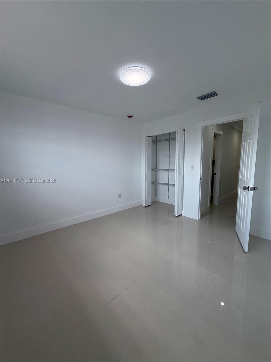 A minimalist bedroom features white walls, light tile flooring, a closet, and an open doorway — 1551 W Okeechobee Rd # 3, Hialeah FL 33010, HIALEAH, FL