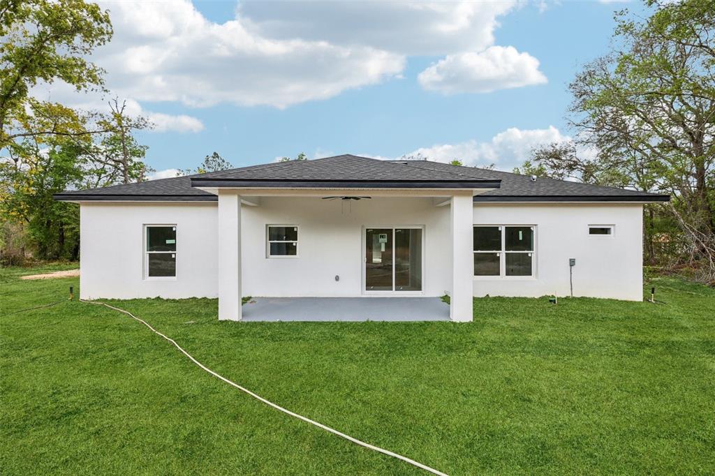 The rear exterior of a white, single-story house with a covered patio and lawn — 15479 SE 115 PLACE ROAD, OCKLAWAHA, FL