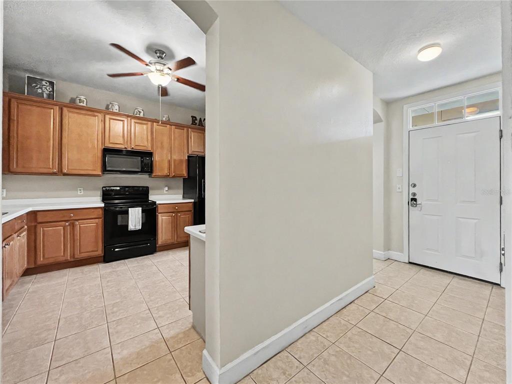 A kitchen with wood cabinets and black appliances sits adjacent to an entryway with tile — 1411 CELEBRATION AVENUE UNIT 309, CELEBRATION, FL