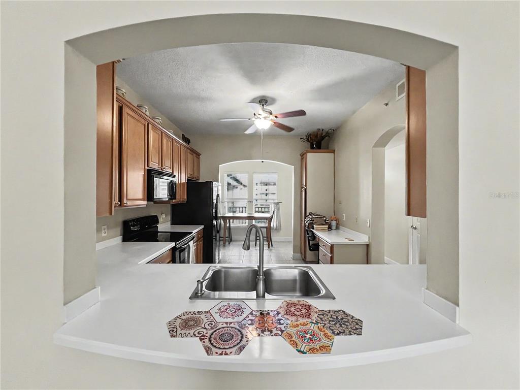 A kitchen view through an arched opening features a sink, wood cabinets, and patterned tiles — 1411 CELEBRATION AVENUE UNIT 309, CELEBRATION, FL