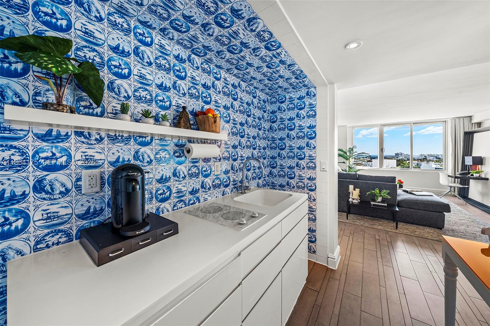 A kitchenette with blue patterned tile walls and white cabinets opens into a living area — 1100 West Ave # 1123, Miami Beach FL 33139, MIAMI BEACH, FL