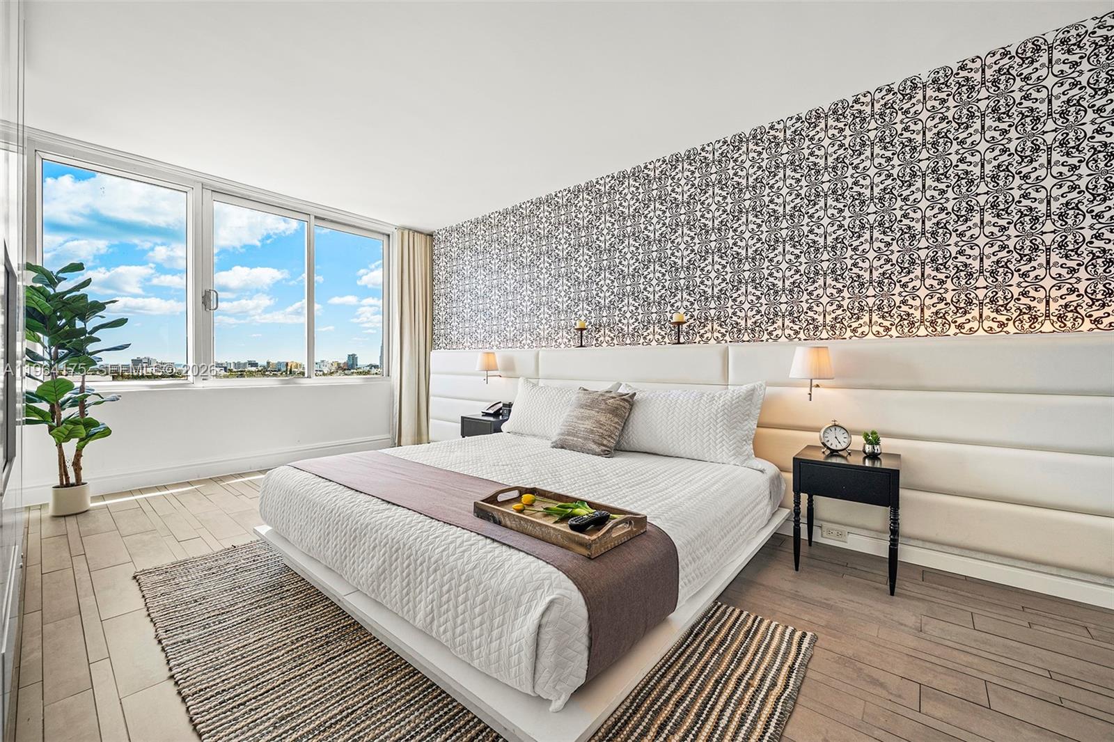 A bedroom features a patterned accent wall, a white upholstered headboard, and a large window — 1100 West Ave # 1123, Miami Beach FL 33139, MIAMI BEACH, FL