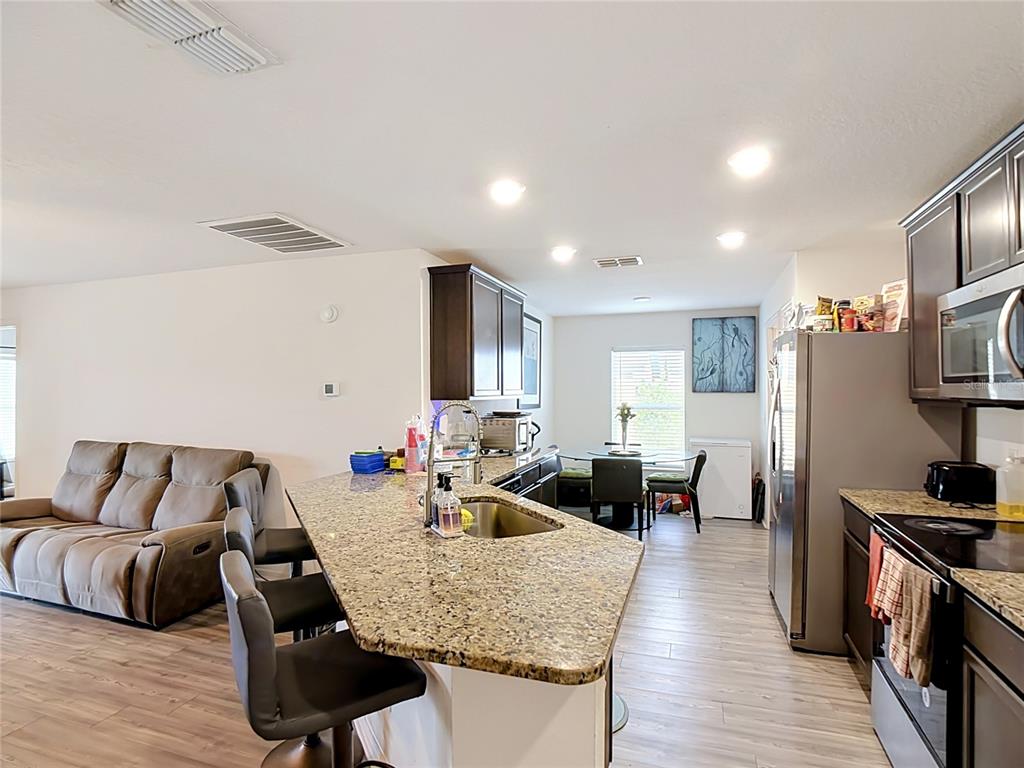 An open-concept kitchen features granite countertops, dark wood cabinetry, and a breakfast bar with stools — 1741 CANAAN LOOP, DUNDEE, FL