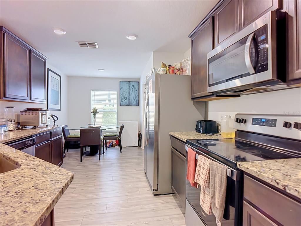 A kitchen with dark wood cabinets, granite countertops, stainless steel appliances, and an adjacent dining area — 1741 CANAAN LOOP, DUNDEE, FL