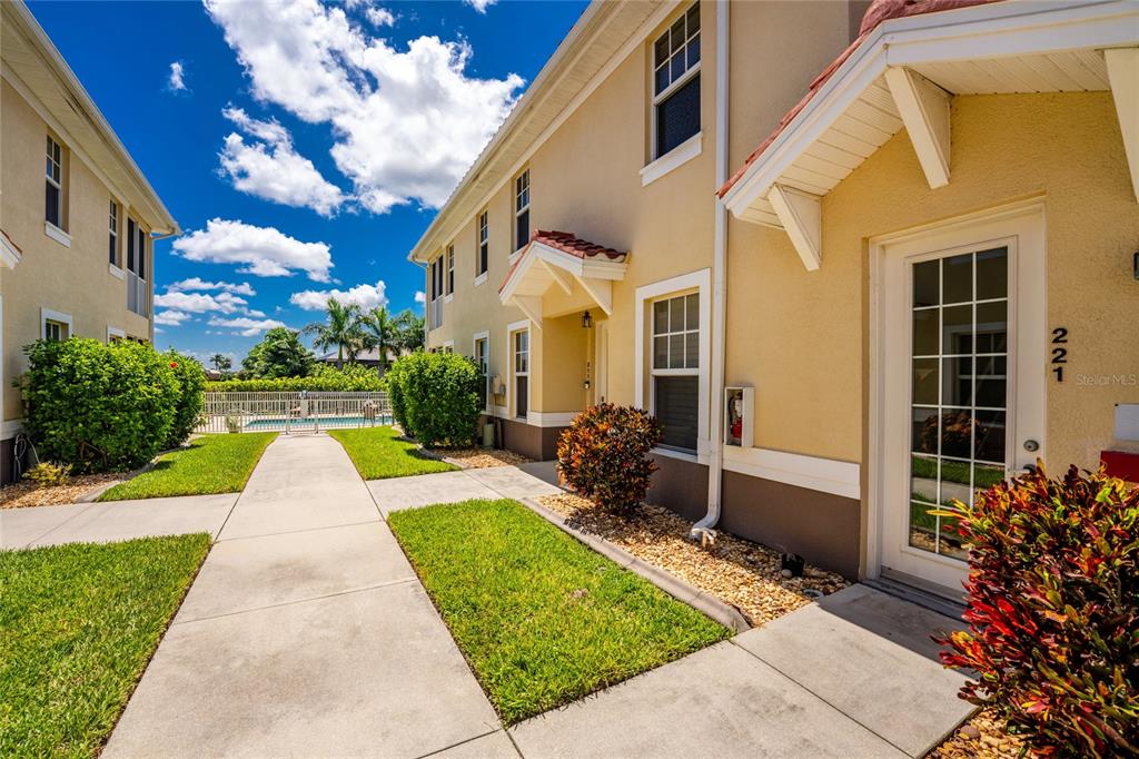 A sidewalk leads past a two-story tan building with a swimming pool in the background — 17210 ACAPULCO ROAD UNIT 221, PUNTA GORDA, FL