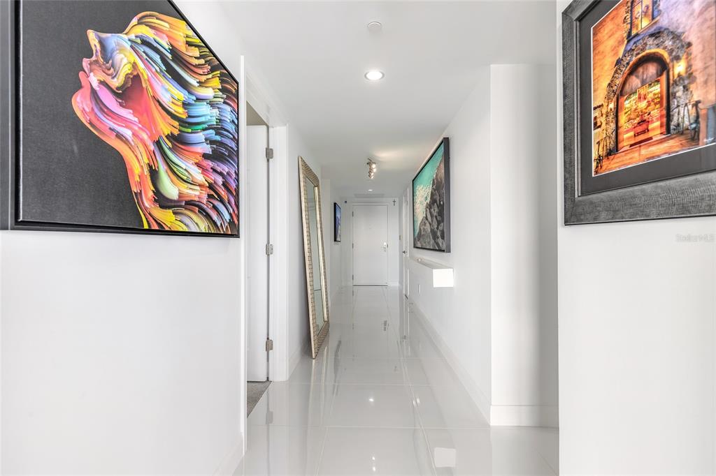 A bright hallway with white walls, glossy tile floors, and framed artwork on both sides — 241 RIVERSIDE DRIVE UNIT 701, HOLLY HILL, FL