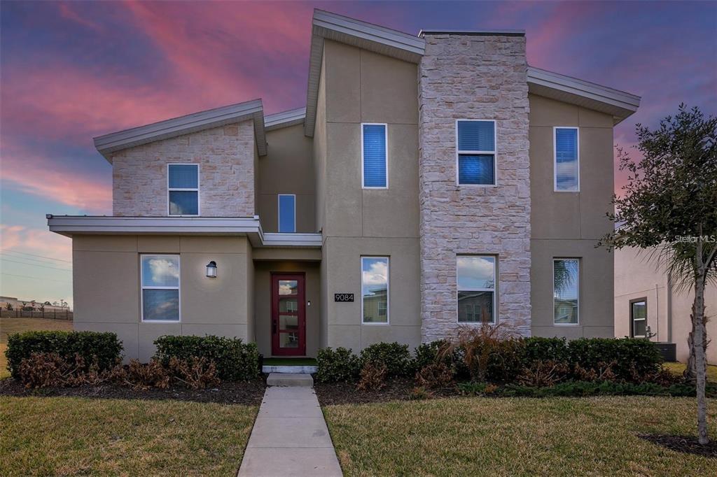 A two-story house features a tan stucco facade, stone accents, and a red front door — 9084 SOMMERSET HILLS DRIVE, DAVENPORT, FL