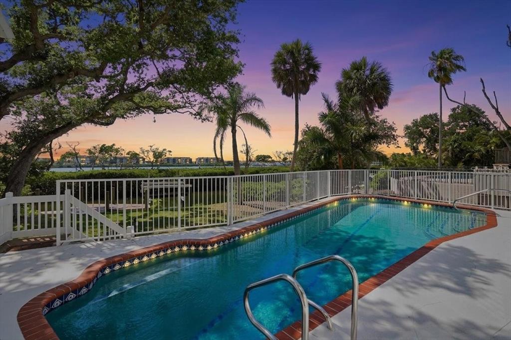 A swimming pool with a red brick border sits in front of a white fence — 3481 BAYOU SOUND, LONGBOAT KEY, FL