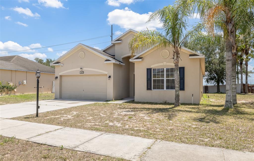A single-story tan stucco house with a two-car garage and a front palm tree — 3216 LYNROCK AVENUE, DUNDEE, FL