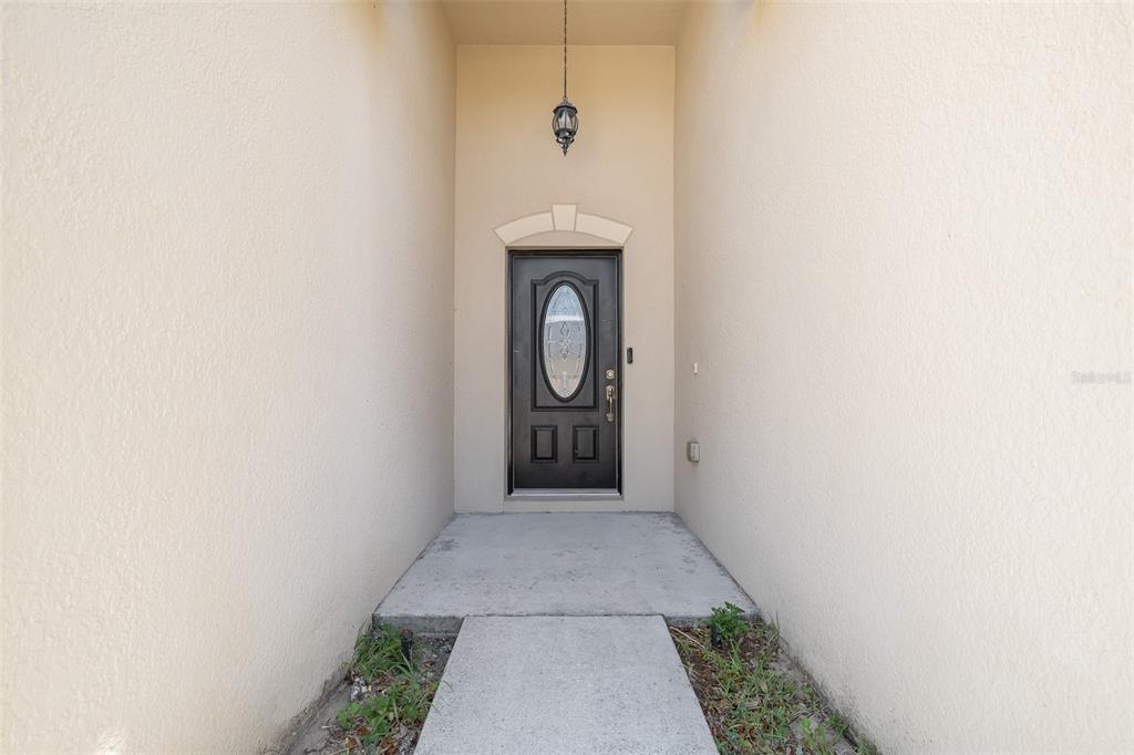 A concrete walkway leads to a dark front door with a glass insert under a portico — 3216 LYNROCK AVENUE, DUNDEE, FL