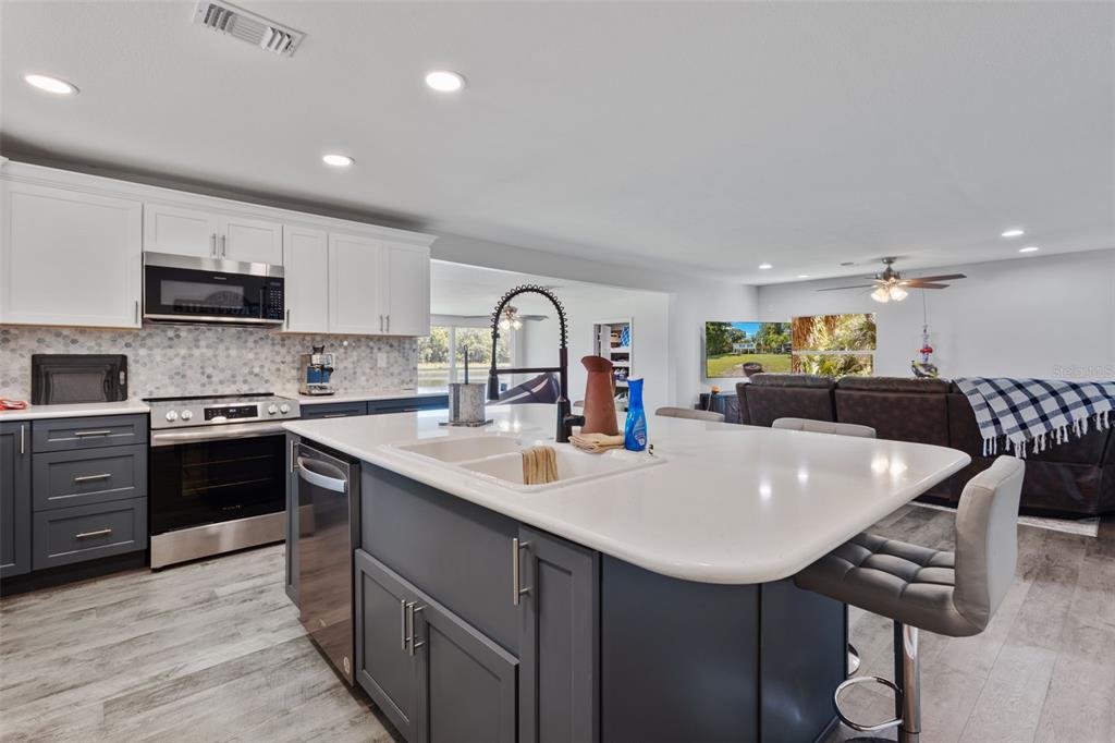 A modern kitchen features a large island with a sink, gray cabinets, and white countertops — 15471 NW 46TH LANE, CHIEFLAND, FL