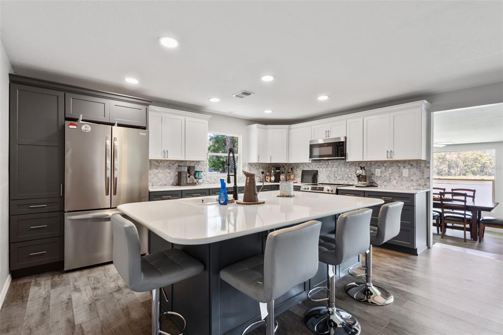 A modern kitchen features a large white island, two-tone cabinetry, and stainless steel appliances — 15471 NW 46TH LANE, CHIEFLAND, FL