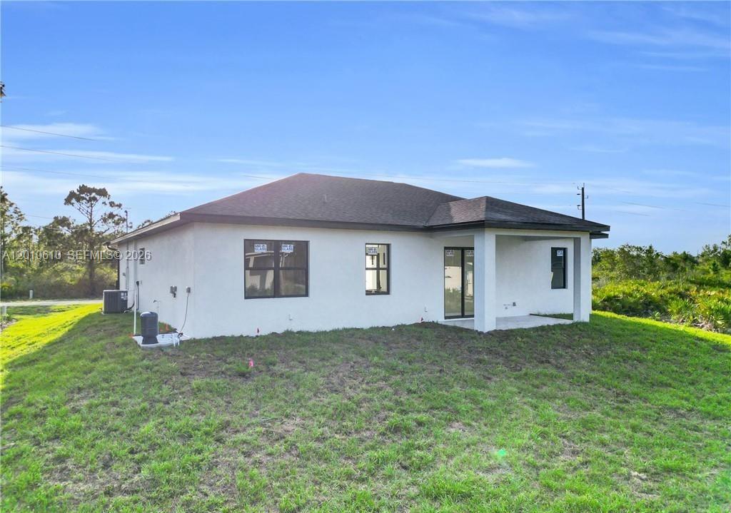 The rear exterior of a single-story house features a covered patio and a grassy yard — 346 Ranchito Ave, Lehigh Acres FL 33974, LEHIGH ACRES, FL