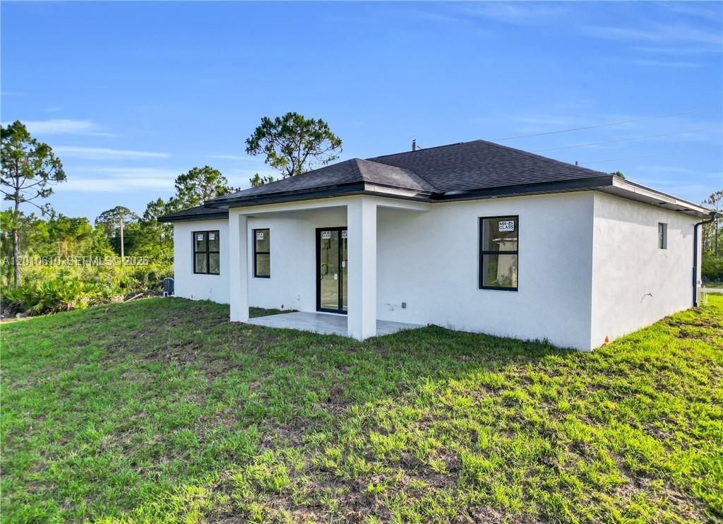 The exterior of a white, single-story house features a covered patio and a grassy yard — 346 Ranchito Ave, Lehigh Acres FL 33974, LEHIGH ACRES, FL
