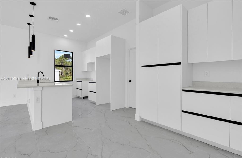 A modern white kitchen features gray marble-look tile flooring and black cabinet hardware — 346 Ranchito Ave, Lehigh Acres FL 33974, LEHIGH ACRES, FL