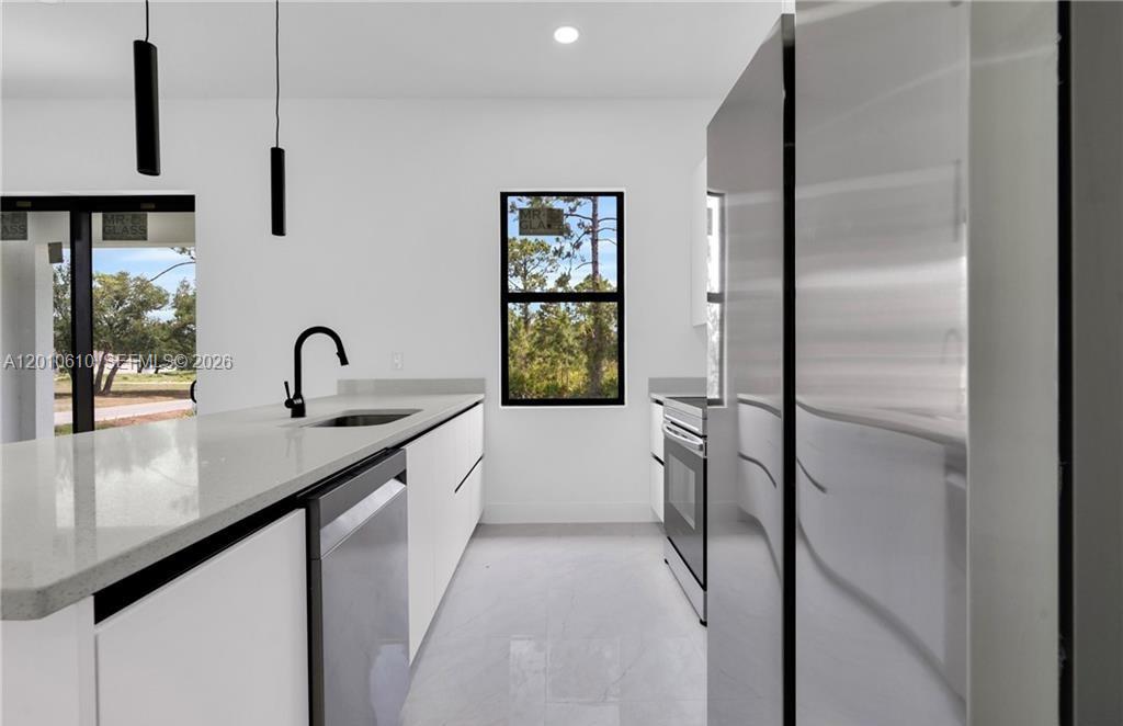 A modern kitchen features white cabinetry, stainless steel appliances, and a large window — 346 Ranchito Ave, Lehigh Acres FL 33974, LEHIGH ACRES, FL