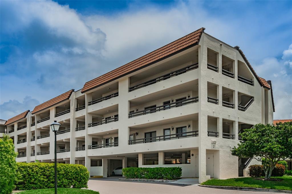 A multi-story apartment building with balconies and covered ground-level parking under a blue sky — 103 1ST STREET E UNIT 313, ST PETERSBURG, FL