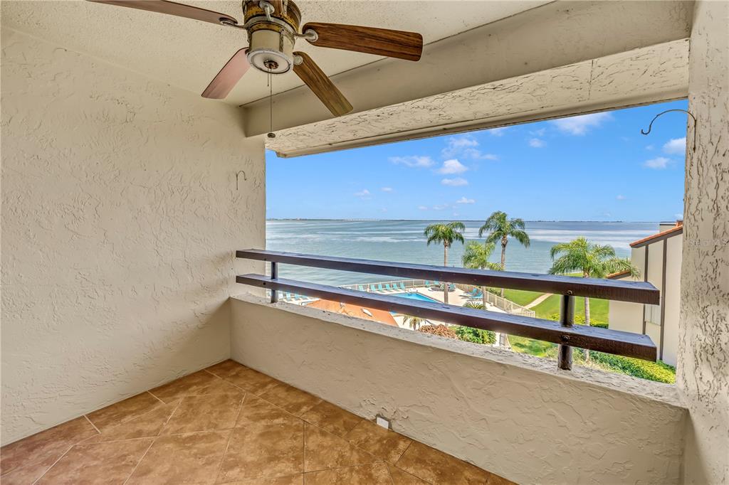 A tiled balcony features a ceiling fan, a wooden railing, and a view of water — 103 1ST STREET E UNIT 313, ST PETERSBURG, FL