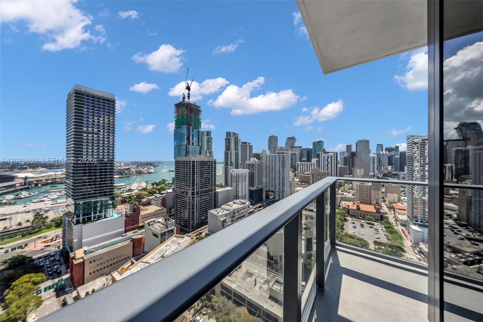 A high-rise balcony overlooks a dense urban skyline with a harbor and construction cranes — 121 NE 5th St # 3401, Miami FL 33132, MIAMI, FL