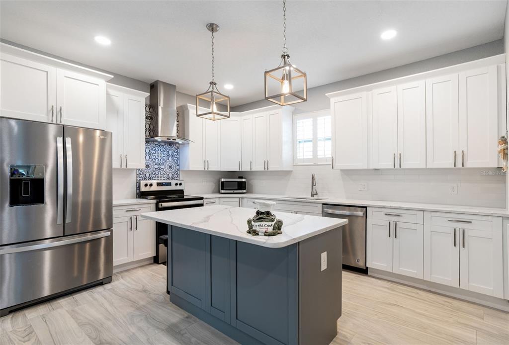 A modern kitchen features white cabinets, a dark blue island, stainless appliances, and patterned backsplash — 4011 55TH AVENUE N, ST PETERSBURG, FL