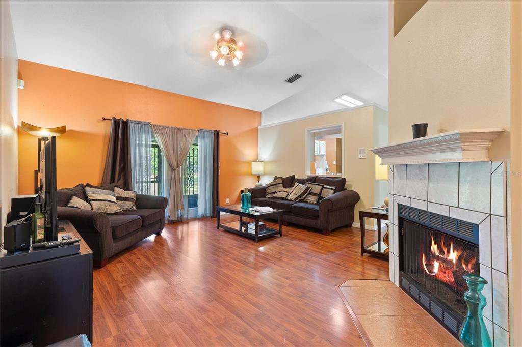 A living room features wood flooring, a fireplace, two dark sofas, and orange accent walls — 7175 COUNTY ROAD 213, WILDWOOD, FL