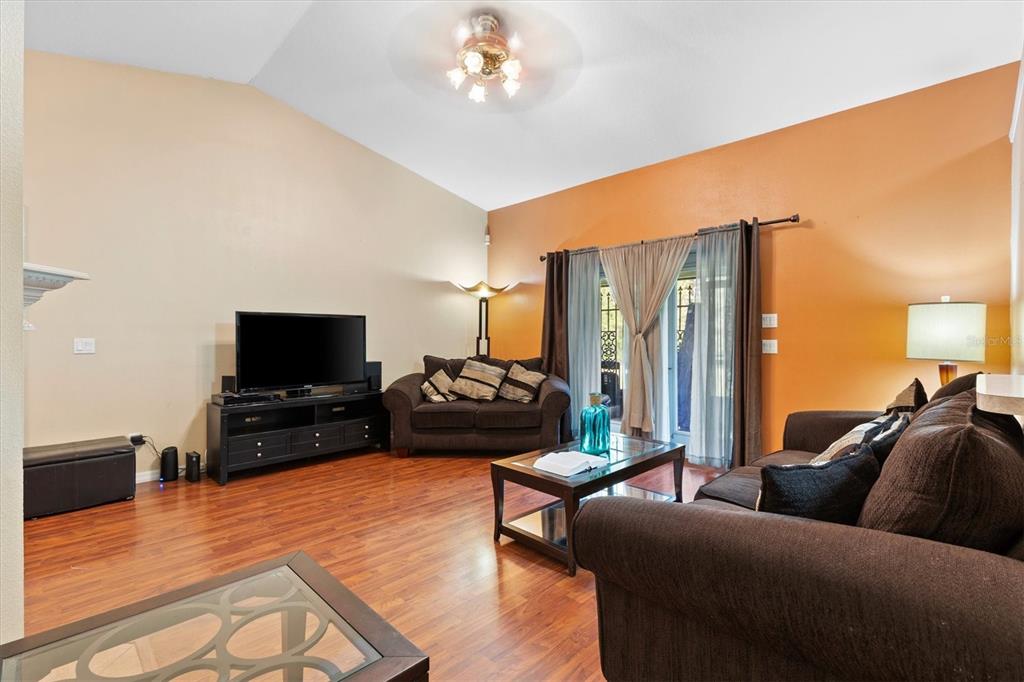 A living room with vaulted ceilings, wood flooring, dark furniture, and an orange accent wall — 7175 COUNTY ROAD 213, WILDWOOD, FL