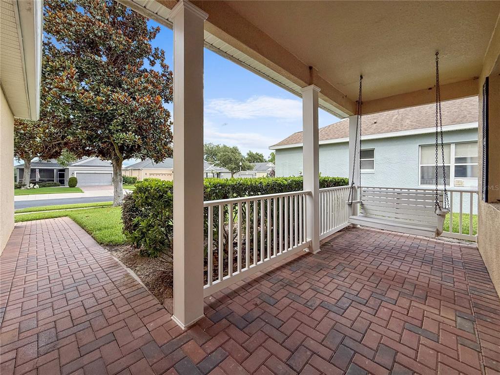 A covered brick patio features a white porch swing and a white railing — 2371 CALEDONIAN STREET, CLERMONT, FL