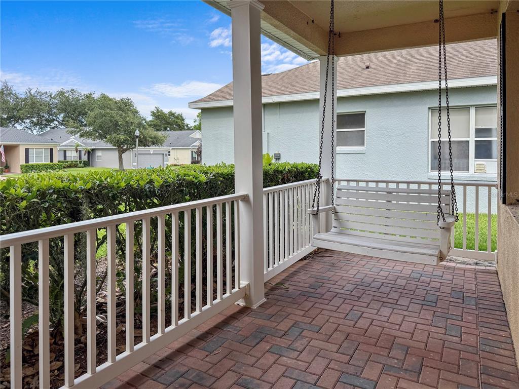 A covered brick patio features a white porch swing and a white railing — 2371 CALEDONIAN STREET, CLERMONT, FL