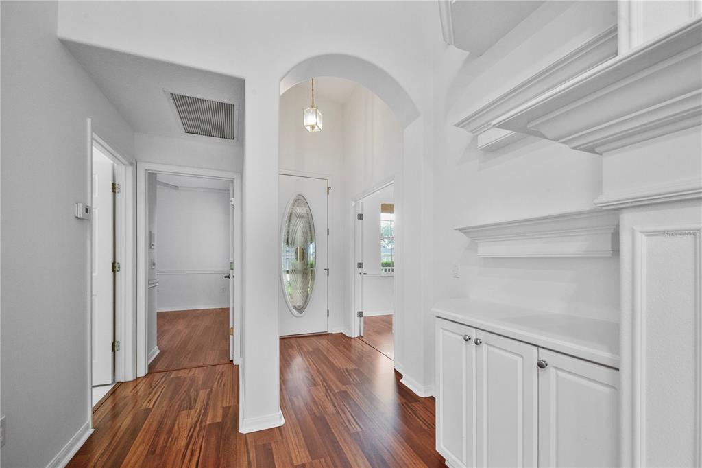 A white-walled entryway features an arched doorway, wood flooring, and built-in white cabinetry — 2371 CALEDONIAN STREET, CLERMONT, FL