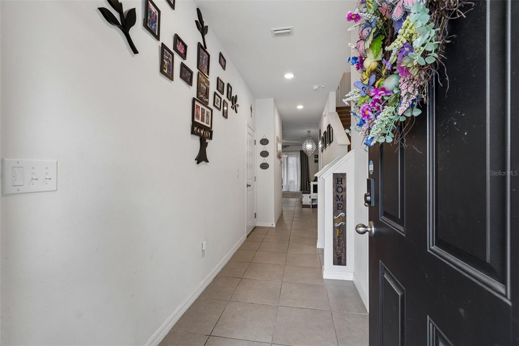 A tiled entryway leads into a hallway with a family photo wall and staircase — 3830 VIGNOBLE LANE, BRANDON, FL