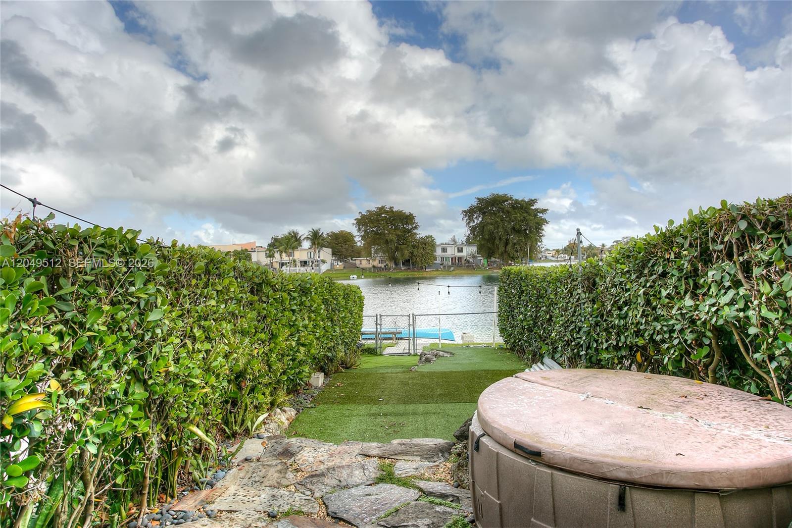A backyard features a hot tub, stone patio, artificial turf, and a view of water — 7389 W 18th Ave # 7389, Hialeah FL 33014, HIALEAH, FL