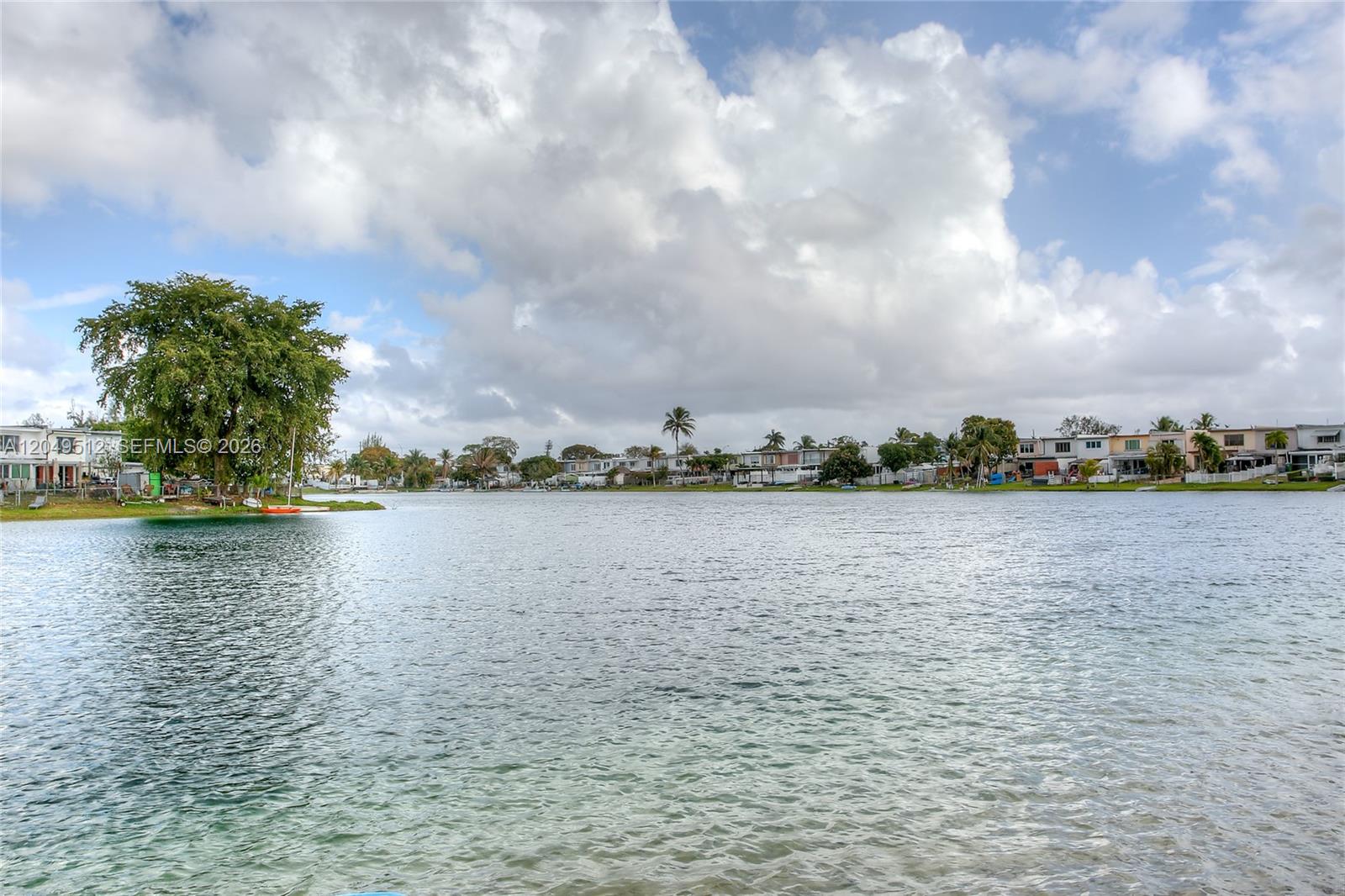 A large lake is surrounded by residential houses and trees under a cloudy sky — 7389 W 18th Ave # 7389, Hialeah FL 33014, HIALEAH, FL
