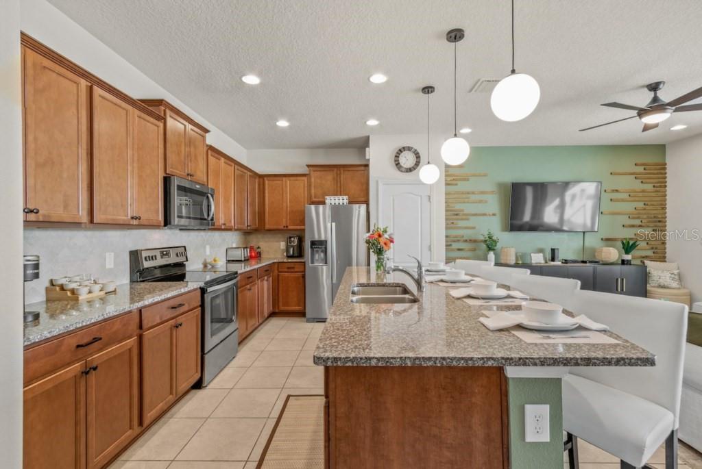 A kitchen island with granite countertops sits in an open-concept living area with lake views — 8838 GENEVE COURT, KISSIMMEE, FL