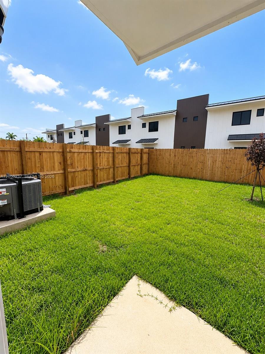 A fenced-in backyard features a patch of green grass and an outdoor air conditioning unit — 552 NW 7th St # 6, Florida City FL 33034, FLORIDA CITY, FL