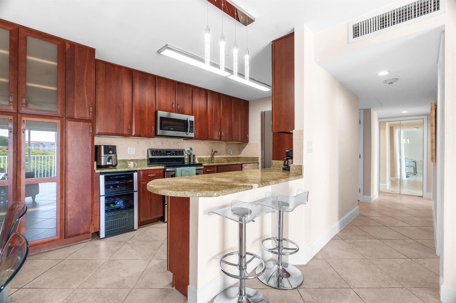 A kitchen features cherry wood cabinets, granite countertops, a wine cooler, and two bar stools — 950 Ponce De Leon Road # 4030, Boca Raton FL 33432, BOCA RATON, FL