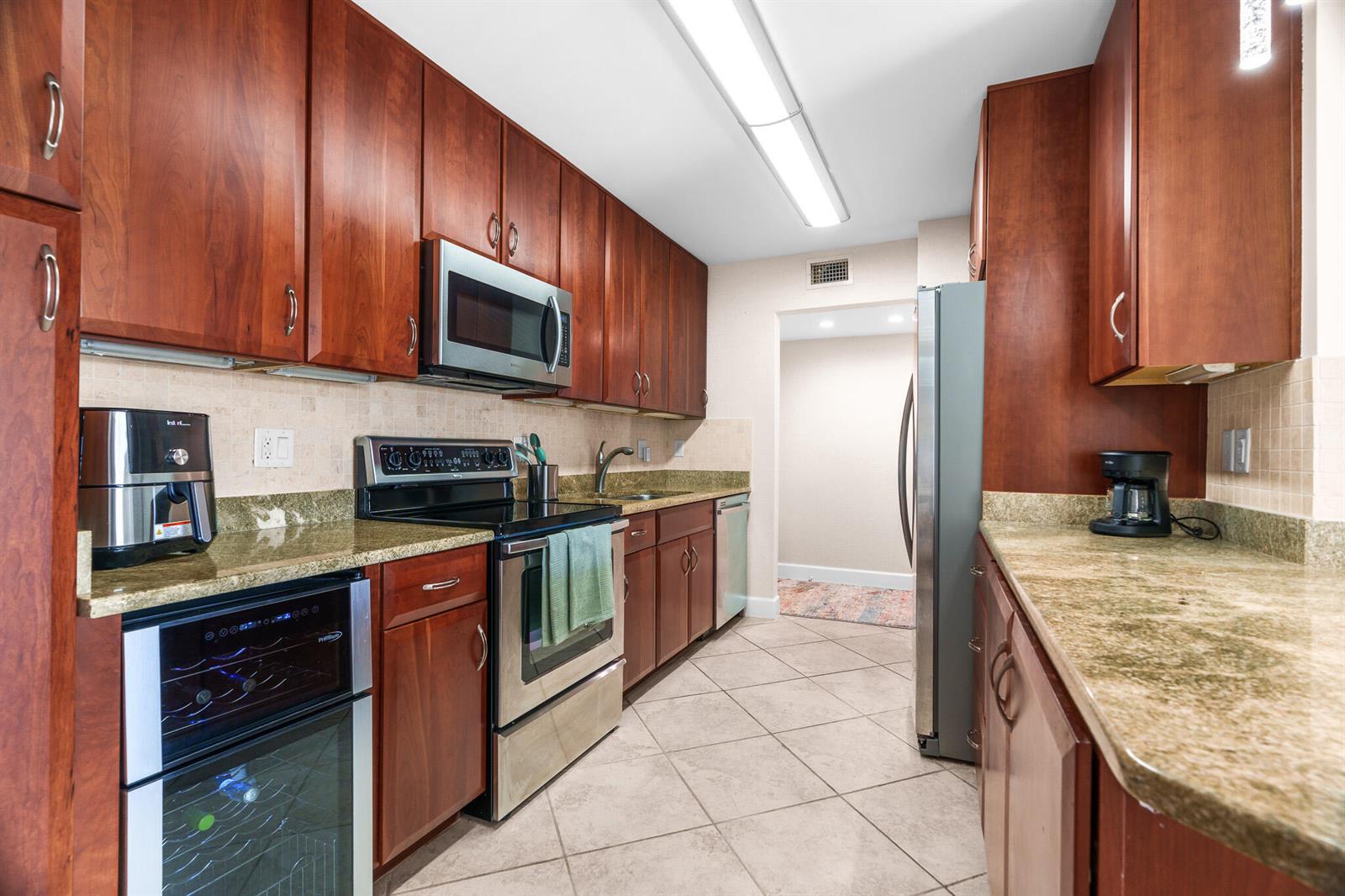 A galley kitchen features cherry wood cabinets, granite countertops, stainless steel appliances, and tile flooring — 950 Ponce De Leon Road # 4030, Boca Raton FL 33432, BOCA RATON, FL